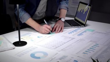 Finansal raporları, çizelgeleri ve hesap tablolarını inceleyen eller iş lambası ve dizüstü bilgisayarla beyaz bir masa üzerinde, iş planlama, bütçe ve yatırım kararları için gece yarısı odaklı analizler