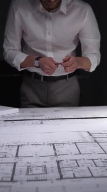 Profesyonel mimar veya mühendis bina tasarımını geliştiriyor, kat planları ve bir masanın üzerinde ölçeklendirilmiş mimari modelle çalışıyor. Gösterişsiz ışıklandırmada mimari ve iş kavramı