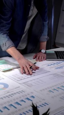 Finansal raporları, çizelgeleri ve hesap tablolarını inceleyen eller iş lambası ve dizüstü bilgisayarla beyaz bir masa üzerinde, iş planlama, bütçe ve yatırım kararları için gece yarısı odaklı analizler