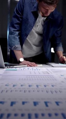 Geç saatlere kadar çalışan girişimci, kağıt, rapor ve dizüstü bilgisayarlardaki iş istatistikleri ve mali verileri analiz ederek, geceleri loş işyerinde kurumsal strateji ve gelecekteki büyümeyi yönetmektedir.