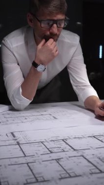 Mühendis ya da mimar, karmaşık bir inşaat projesi üzerinde çalışarak ayrıntılı bina planları ve planlarına yoğunlaşıyor. Gösterişsiz ışıklandırmada mimari ve iş kavramı