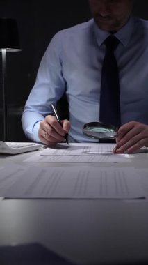 Mali denetçi, belgeleri büyüteç ve hesap makinesiyle analiz ediyor. İş hayatında detaylara, doğruluğa ve kapsamlı soruşturmaya odaklan. İş dünyasında denetim ve vergi teması