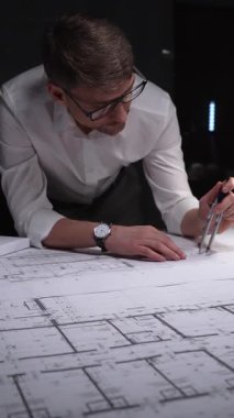 Mimari planlar üzerinde geç saatlere kadar çalışan mühendis, inşaatın detaylarını ölçmek ve çizmek için bir pusula kullanıyor. Gösterişsiz ışıklandırmada mimari ve iş kavramı