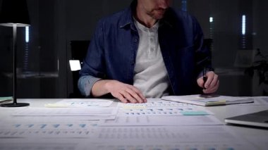 Geç saatlere kadar çalışan, ofis masasındaki dizüstü bilgisayardaki mali verileri ve iş raporlarını analiz eden, performans grafiklerini inceleyen ve planlama stratejisini lamba ışığında inceleyen, kurumsal büyümeyi yönlendiren bir adam.