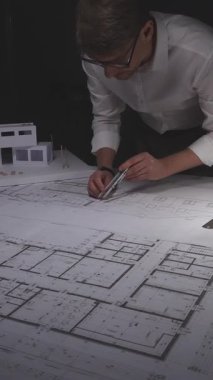 Mimar, bina planları, bir bina modeli ve mimari ve mühendislik planları ile ilgili ayrıntıları çiziyor. Gösterişsiz ışıklandırmada mimari ve iş kavramı