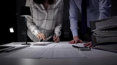 Evrak ve mali veriler üzerinde işbirliği yapan iş adamları, önemli belgeleri incelemek, projeleri yönetmek ve ticari başarı için kapsamlı bir analiz sağlamak için ofiste geç saatlere kadar kalırlar.