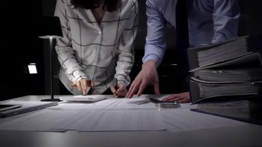 Evrak ve mali veriler üzerinde işbirliği yapan iş adamları, önemli belgeleri incelemek, projeleri yönetmek ve ticari başarı için kapsamlı bir analiz sağlamak için ofiste geç saatlere kadar kalırlar.