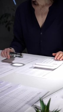 Mali raporları ve açıklamaları analiz eden bir muhasebeci, hesap makinesi ve büyüteç kullanarak denetim ve bütçe verilerini gözden geçirir. İş dünyasında denetim ve vergi teması