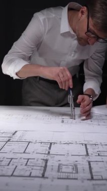 Adam mimari planlara odaklanıyor, yeni bir proje çözümü için kesin ölçümler hazırlıyor. Gösterişsiz ışıklandırmada mimari ve iş kavramı