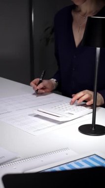 Kadınların elleri hesap makinesi kullanıyor ve loş bir ofis masasında mali evraklara yazı yazıyor. Bütçeleri, harcamaları ve raporları akşam geç saatlerde analiz ediyor. İş dünyasında denetim ve vergi teması