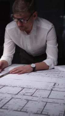 Mimari tasarımlar üzerinde çalışan erkek mimar, büyük kağıt kağıtlara dikkatlice ölçüyor ve kat planlarını çiziyor. Gösterişsiz ışıklandırmada mimari ve iş kavramı