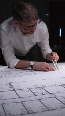 Mimari planlar üzerinde geç saatlere kadar çalışan mühendis, inşaatın detaylarını ölçmek ve çizmek için bir pusula kullanıyor. Gösterişsiz ışıklandırmada mimari ve iş kavramı