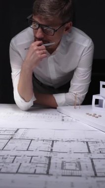 Yeni modern ev tasarımı gelişimi için mimari tasarım planlarını ve beyaz fiziksel modeli derinden düşünen bir mimar. Gösterişsiz ışıklandırmada mimari ve iş kavramı