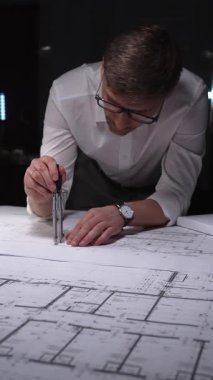 Mimari planlar üzerinde geç saatlere kadar çalışan mühendis, inşaatın detaylarını ölçmek ve çizmek için bir pusula kullanıyor. Gösterişsiz ışıklandırmada mimari ve iş kavramı