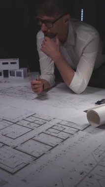 Planlar ve mimari model üzerinde çalışan mimar, yeni bir bina projesi planlıyor, tasarım ve mühendislik planlarına odaklanıyor. Gösterişsiz ışıklandırmada mimari ve iş kavramı