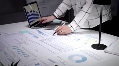 İşadamı karanlık bir ofisteki bir masaya odaklanmış, dizüstü bilgisayardaki mali raporları ve çizelgeleri analiz ediyor, gece yarısı üretkenlik oturumunda iş akışını yönetiyor.