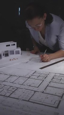 Kadın mimar ölçekli bir model inşa ediyor ve karanlık bir ofiste daire ya da ev tasarımı için kat planları çiziyor. Gösterişsiz ışıklandırmada mimari ve iş konsepti