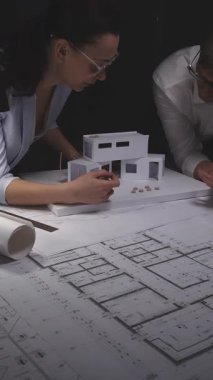 Mimarlar modern bir ev modeli tasarlıyor, yeni bir konut projesinin mimari planlarını tartışıyor, planlar üzerinde çalışıyorlar. Gösterişsiz ışıklandırmada mimari ve iş kavramı