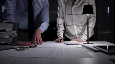 Evrak ve mali veriler üzerinde işbirliği yapan iş adamları, önemli belgeleri incelemek, projeleri yönetmek ve ticari başarı için kapsamlı bir analiz sağlamak için ofiste geç saatlere kadar kalırlar.