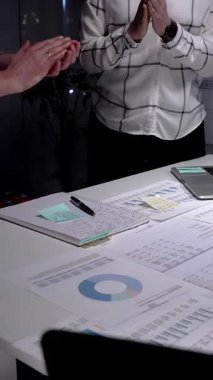 İş arkadaşları, mali belgeler, çizelgeler, tablet ve lambayla kaplı ofis masasını alkışlayarak, gece yarısı yapılan analizlerden sonra anlaşmaya işaret ediyor ve başarılı sonuçları kutluyorlar.