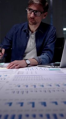 Gece geç saatlere kadar karanlık bir ofiste çalışan meşgul bir adam, stratejik planlama ve fazla mesai üretkenliği için dijital tablet kullanan finansal veriler, piyasa analizleri ve iş raporları üzerinde yoğunlaşıyor.