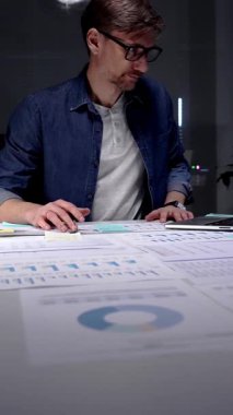 Gece geç saatlere kadar karanlık bir ofiste çalışan meşgul bir adam, stratejik planlama ve fazla mesai üretkenliği için dijital tablet kullanan finansal veriler, piyasa analizleri ve iş raporları üzerinde yoğunlaşıyor.