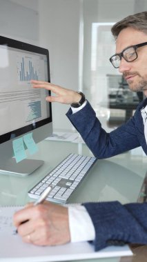 Profesyonel iş adamı gözlük takıyor ve spor ceket giyiyor, çağdaş bir ofis ortamında çalışıyor, bir masaüstü bilgisayarında görevler yapıyor. İş adamları konsepti