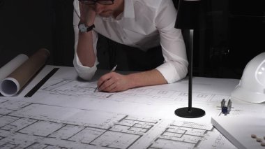 Çok çalışan mimar gece yarısı çalışırken baş ağrısı ve stres hissederek inşaat planları ve tasarım yapmayı planlıyor..