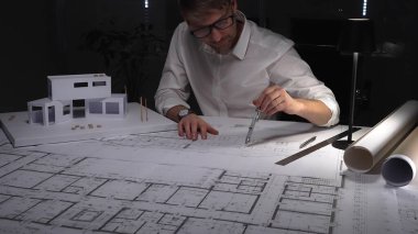 Mimar planlar üzerinde yoğunlaşır, titizlikle yeni bir ev projesi için tasarımlar hazırlar, fiziksel bir model üzerinde çalışır. İş ve mimarlık kavramı