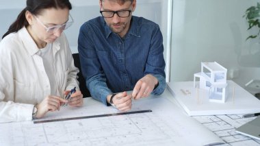 Mimarlar yeni bir yapı projesi geliştiriyor, tasarım detayları üzerinde işbirliği yapıyor ve tartışıyorlar, planlar, ölçekli bir model ve inşaatı planlamak için araçlar kullanıyorlar