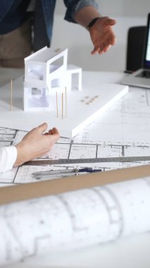 Mimarlar yeni bir bina projesi geliştiriyorlar. Meslektaşları mimari bir model, sergilenen tasarım, planlama ve takım çalışması üzerinde cetvelle çalışan bir kadın profesyonel çizim.