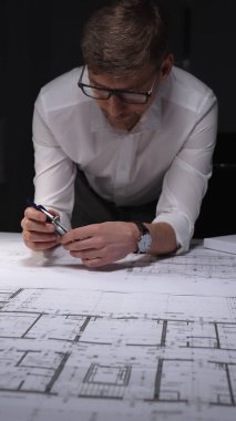 Mimari planlar üzerinde geç saatlere kadar çalışan mühendis, inşaatın detaylarını ölçmek ve çizmek için bir pusula kullanıyor. Gösterişsiz ışıklandırmada mimari ve iş kavramı