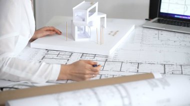 İnşaat planları ve çağdaş bir yapı modeli üzerinde çalışan kadın mimar, masasında yenilikçi tasarımlar ve kentsel kalkınma stratejileri kavramlaştırıyor.