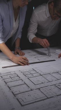 Modern bir ev tasarımında işbirliği yapan mimarlar, bir masaüstünde ölçekli bir model ve mühendislik planlarıyla çalışıyorlar. Gösterişsiz ışıklandırmada mimari ve iş kavramı.