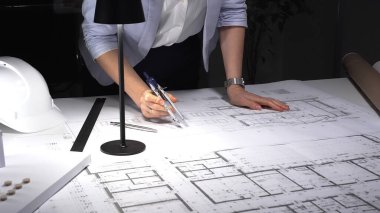 Mimar eller pusulayı kullanarak sabit şapkalı, lambalı ve yuvarlak planlı bir masanın planına kesin çizgiler çizer ve ölçer..