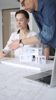 Mimarlar yeni bir bina projesi geliştiriyorlar. Meslektaşları mimari bir model, sergilenen tasarım, planlama ve takım çalışması üzerinde cetvelle çalışan bir kadın profesyonel çizim.