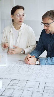 Planlar ve dizüstü bilgisayarlar üzerinde işbirliği yapan mimarlar, teknik çizimlere işaret ediyor ve bir bina projesi için çağdaş bir ofis toplantısında yapısal planlar ve tasarım ayrıntılarını tartışıyor