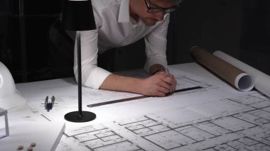 Gece mimari planlar çizen mimar, bir masa lambasıyla aydınlatılıyor, bina tasarımı ve mühendisliğine odaklanıyor. İş ve mimarlık kavramı