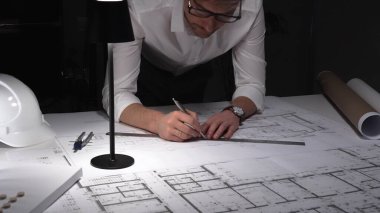 Gece mimari planlar çizen mimar, bir masa lambasıyla aydınlatılıyor, bina tasarımı ve mühendisliğine odaklanıyor. İş ve mimarlık kavramı