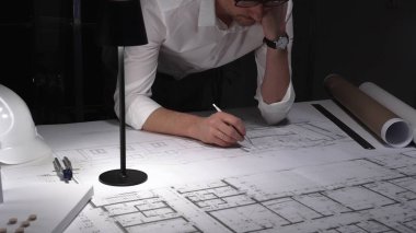 Çok çalışan mimar gece yarısı çalışırken baş ağrısı ve stres hissederek inşaat planları ve tasarım yapmayı planlıyor..