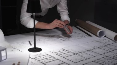 Mimar eller dikkatlice tasarım çizer, inşaat projesini planlar. Mühendislik uzmanı ofiste planlar üzerinde çalışıyor. İş ve mimarlık kavramı