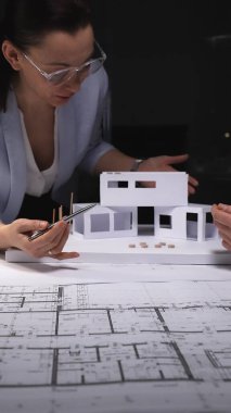 Mimarlar konut tasarımı projesinde işbirliği yapıyorlar, mimari planlardan minyatür bir kağıt ev modeli inşa ediyorlar. Gösterişsiz ışıklandırmada mimari ve iş kavramı