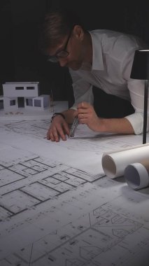 Profesyonel mimar, ayrıntılı teknik çizim ve yapısal tasarıma odaklanarak pusula ile planı ölçüyor. Gösterişsiz ışıklandırmada mimari ve iş kavramı