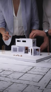Mimarlar konut inşaatı tasarlar, ofis masasında kağıt modelli planlar analiz ederler, inşaat projesini geliştirirler. Mimarlık ve iş kavramı gösterişsiz ışıklandırmada