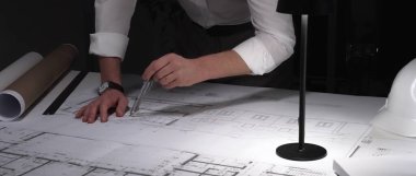 Mimar eller dikkatlice tasarım çizer, inşaat projesini planlar. Mühendislik uzmanı ofiste planlar üzerinde çalışıyor. İş ve mimarlık kavramı