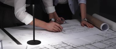 Architects collaborating in office late at night, focused on detailed planning of building design and construction project. Professional teamwork and deadline concept.