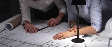 Mimarlar birlikte çalışır, bina planlarını ve planlarını analiz eder, bir ofiste tasarım kavramlarını ve mühendislik unsurlarını tartışırlar..