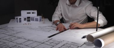 Mimar planlar üzerinde yoğunlaşır, titizlikle yeni bir ev projesi için tasarımlar hazırlar, fiziksel bir model üzerinde çalışır. İş ve mimarlık kavramı