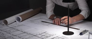 Gece mimari planlar çizen mimar, bir masa lambasıyla aydınlatılıyor, bina tasarımı ve mühendisliğine odaklanıyor. İş ve mimarlık kavramı