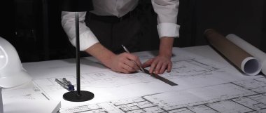 Mimar eller dikkatlice tasarım çizer, inşaat projesini planlar. Mühendislik uzmanı ofiste planlar üzerinde çalışıyor. İş ve mimarlık kavramı